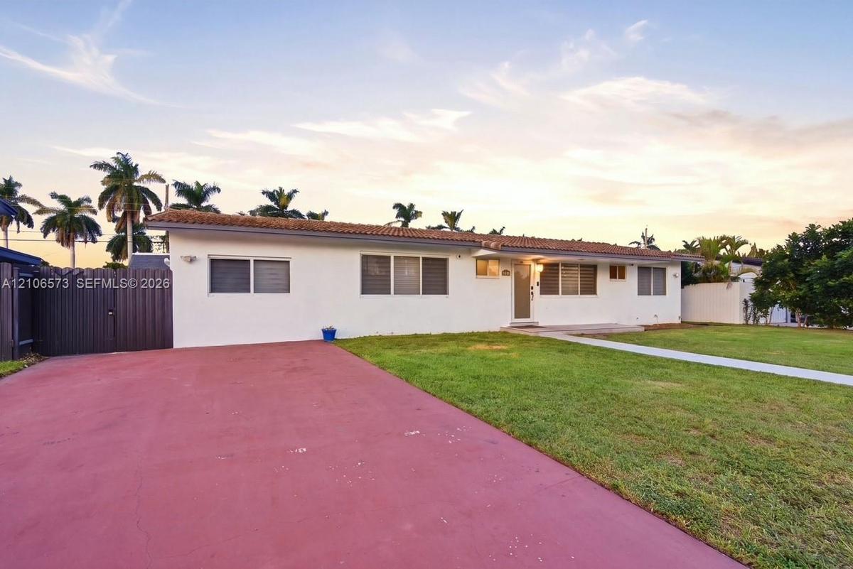 Single-story residence featuring a tile roof, light-colored exterior finish, expansive paved driveway, and manicured lawn