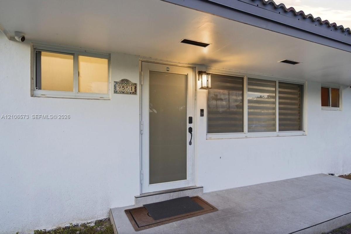 Exterior entry featuring a covered concrete porch, a frosted glass-panel front door, horizontal sliding windows, and a structured tile roofline