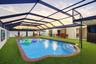 In-ground pool with brick coping, enclosed by a full-coverage metal screen lanai over artificial turf surfacing