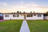 Single-story exterior featuring a low-pitched clay tile roof, white stucco facade, concrete walkway, and integrated front entry porch