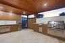 Covered outdoor kitchen featuring vertical wood-slat cabinetry, expansive stone countertops, stainless steel built-in grill, integrated sink, and rece