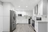 Kitchen featuring white shaker-style cabinetry, stainless steel appliances, stone-look backsplash, wood-finish flooring, and recessed ceiling lighting