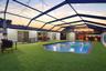 Screened-in outdoor living space featuring an in-ground swimming pool with brick coping, synthetic turf lawn, and a built-in outdoor bar