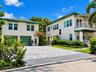 Two-story exterior featuring multi-tone paver driveway, green-tinted garage doors, striped fabric awnings, a second-story balcony with white railing, 