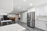 Kitchen featuring white cabinetry, solid-surface countertops, stone-patterned backsplash, stainless steel refrigerator, and wood-finish flooring