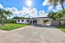 Single-story exterior featuring a painted stucco facade, attached covered carport, concrete driveway, and decorative breeze block privacy screen
