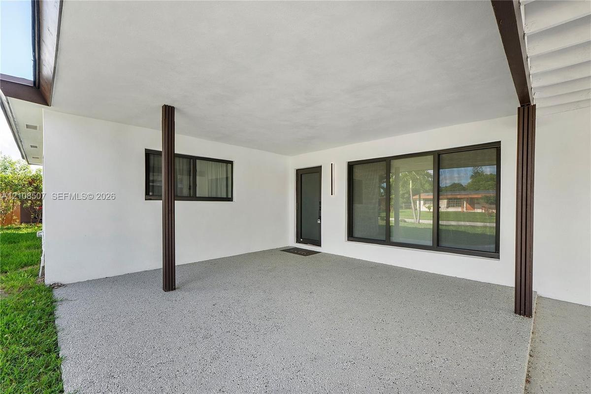 Covered patio featuring an aggregate concrete floor, dark-finished structural support columns, a glass-panel entry door, and large-format multi-pane w