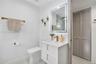 White vanity with a rectangular sink, quartz-style countertop, brass-finish faucet and hardware, LED-backlit mirror, and louvered-panel closet doors