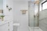 Floating vanity with integrated sink, brass hardware, walk-in shower with glass enclosure, wall-mounted rainfall showerhead, and tile-surround shower 
