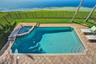 In-ground pool with an integrated spa, paver deck, metal fencing, and grass lawn bordering the water
