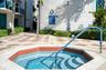 Octagonal in-ground spa featuring a tiled interior, stone coping, a built-in safety handrail, and an exterior shower fixture situated on a paved patio