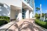 High-rise exterior featuring concrete structural pillars, floor-to-ceiling glass windows, a brick paver driveway, and manicured landscaping