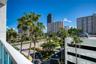 Exterior balcony with white metal railings, overlooking an urban streetscape featuring mature palm trees and high-rise architecture