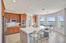 Kitchen featuring shaker-style cabinetry, quartz countertops, a central island with an integrated sink, built-in stainless steel double ovens, and wat