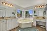 Bathroom featuring a corner soaking tub, dual vanity with stone countertops, integrated makeup vanity, and two large wall-mounted mirrors