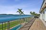 Elevated terrace with tile flooring and metal railings, overlooking a rectangular swimming pool, manicured lawn, and waterfront expanse
