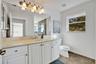 Bathroom featuring a white vanity with integrated basin, expansive wall-mounted mirror, five-light overhead fixture, and tile flooring