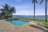 In-ground pool with stone-accented spillover spa, expansive paver patio, metal perimeter fencing, and mature palm trees overlooking the lake