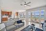 Open-concept living space featuring wood-finish cabinetry, a waterfall-edge center island with a built-in sink, recessed lighting, a modern ceiling fa
