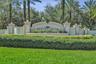 Stucco community signage featuring decorative masonry pillars, integrated lighting fixtures, tiered architectural detailing, and mature palm landscapi