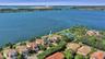 Aerial perspective of waterfront property featuring extensive shoreline access, tile roof construction, and proximity to community-maintained tennis c