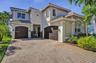Two-story exterior featuring a paver driveway, multi-pane windows, arched garage openings, and a tile roof