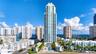 High-rise residential tower featuring tiered glass balconies, an expansive ground-level swimming pool, and stone-paved pool deck