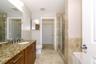 Bathroom featuring a vanity with stone-finish countertop, undermount sink, shower with glass enclosure and stone-finish tile surround, and tile floori