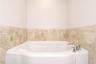 Built-in soaking tub with a polished chrome deck-mounted faucet, surrounded by neutral-toned stone tile wainscoting