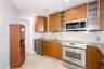 Kitchen featuring natural wood-finish cabinetry, stone-surface countertops, stainless steel appliances, glass-panel cabinet inserts, and tile flooring
