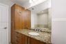 Wood-finish cabinetry with integrated tall storage, stone-surfaced vanity top, undermount sink, and large wall-mounted mirror