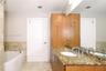 Bathroom featuring stone-surface vanity with dual integrated sinks, floor-to-ceiling wood cabinetry, large wall-mounted mirror, and a soaking tub with