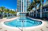 In-ground swimming pool with multi-level entry steps, expansive stone paver deck, and mature palm trees