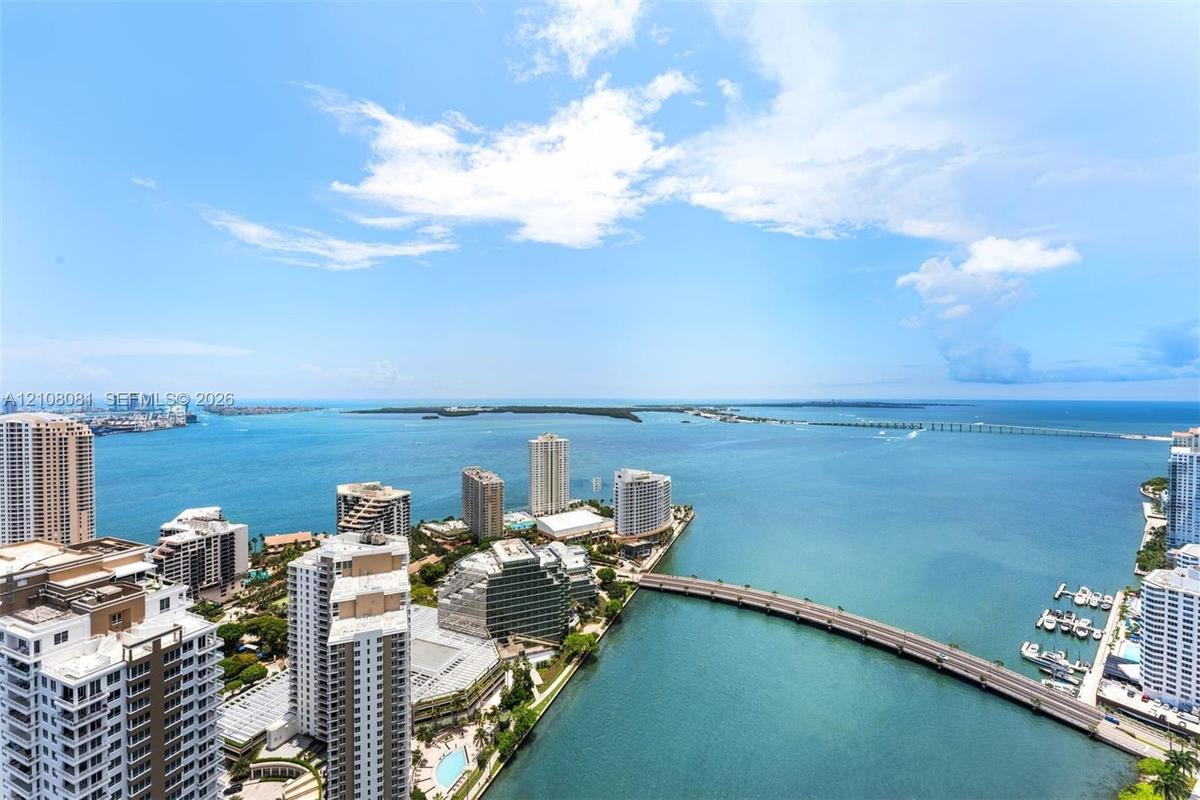 Elevated perspective featuring coastal water, bridge infrastructure, high-rise urban density, and open horizon