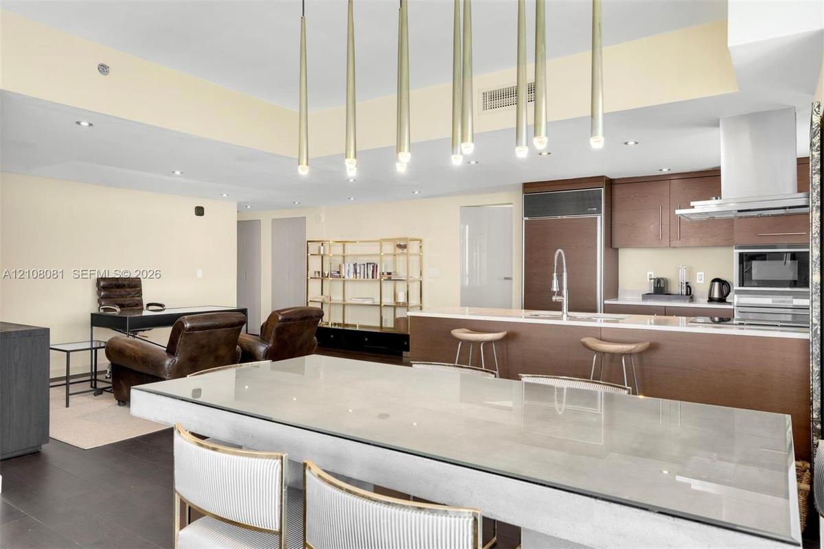 Open concept kitchen featuring dark wood-finish cabinetry, built-in stainless steel appliances, a center island with a stone countertop, and custom mu