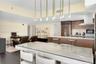 Open concept kitchen featuring dark wood-finish cabinetry, built-in stainless steel appliances, a center island with a stone countertop, and custom mu