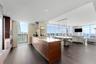 Kitchen featuring flat-panel wood cabinetry, stone countertops, stainless steel appliances, wood-finish flooring, and floor-to-ceiling windows