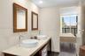 Dual-basin vanity featuring white vessel sinks, quartz countertops, chrome high-arc faucets, and wood-framed mirrors