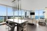Floor-to-ceiling windows, wood-finish flooring, and a linear pendant light fixture featuring multiple metallic cylindrical elements