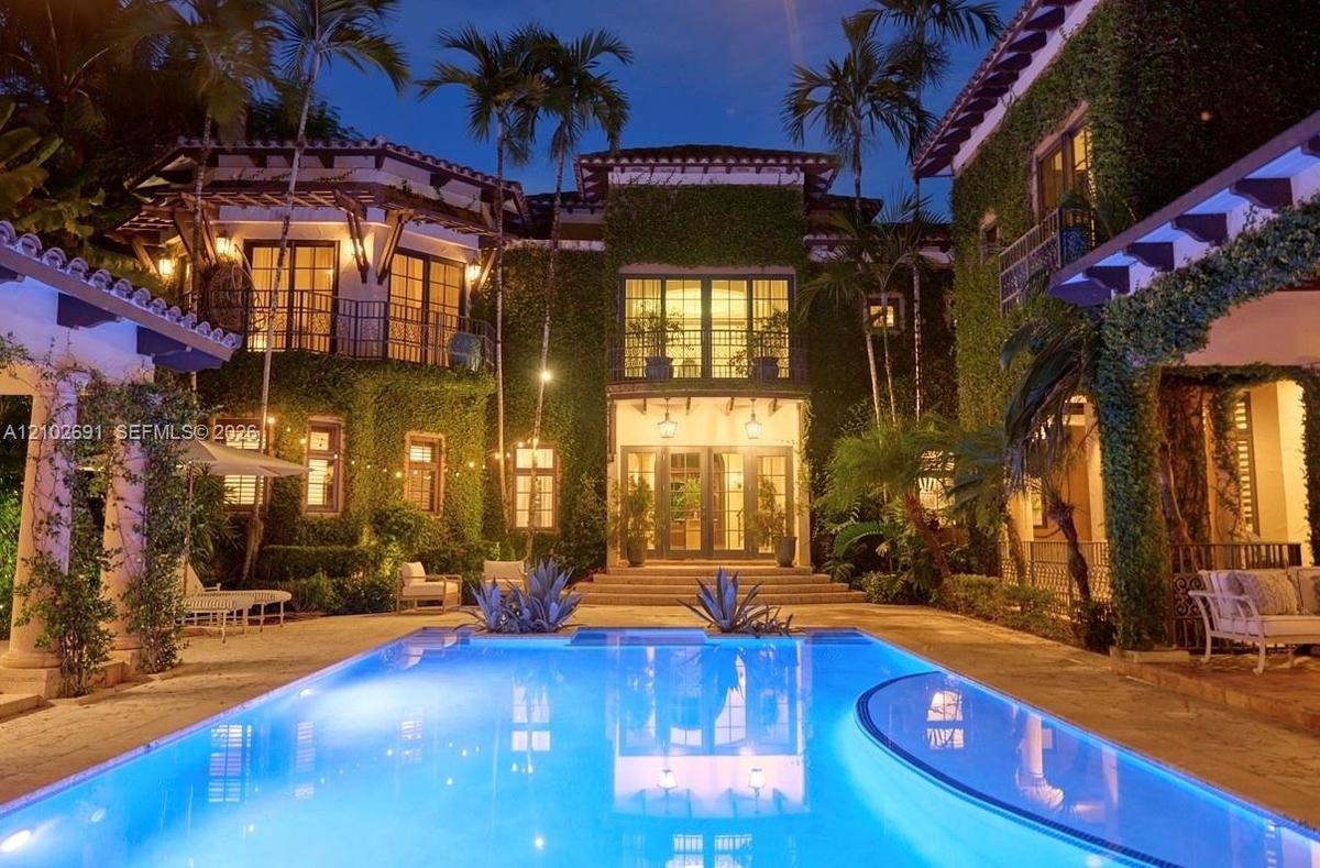 Mediterranean-style estate featuring an ivy-clad exterior, multi-level balconies, stone-paved patio, and a rectangular in-ground swimming pool with an