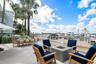 Waterfront stone patio featuring built-in outdoor kitchen, metal railing, and mature palm trees