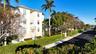 Multi-story stucco exterior featuring a hip roof, arched entryway, private balconies, and landscaped grounds with mature palm trees
