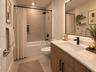 Bathroom featuring a wood-finish vanity with a quartz countertop, recessed shower niche, oversized backlit mirror, and matte black plumbing fixtures