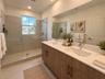 Double vanity with wood-finish cabinetry, quartz countertops, undermount sinks, full-width wall mirror, and a walk-in shower with floor-to-ceiling til