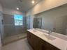 Dual-sink vanity with a white countertop and wood-finish cabinetry, frameless glass-enclosed shower featuring tile walls, integrated shower niche, and