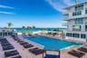 In-ground rectangular swimming pool surrounded by a brick paver deck, multi-story building with private railed balconies, and direct oceanfront access