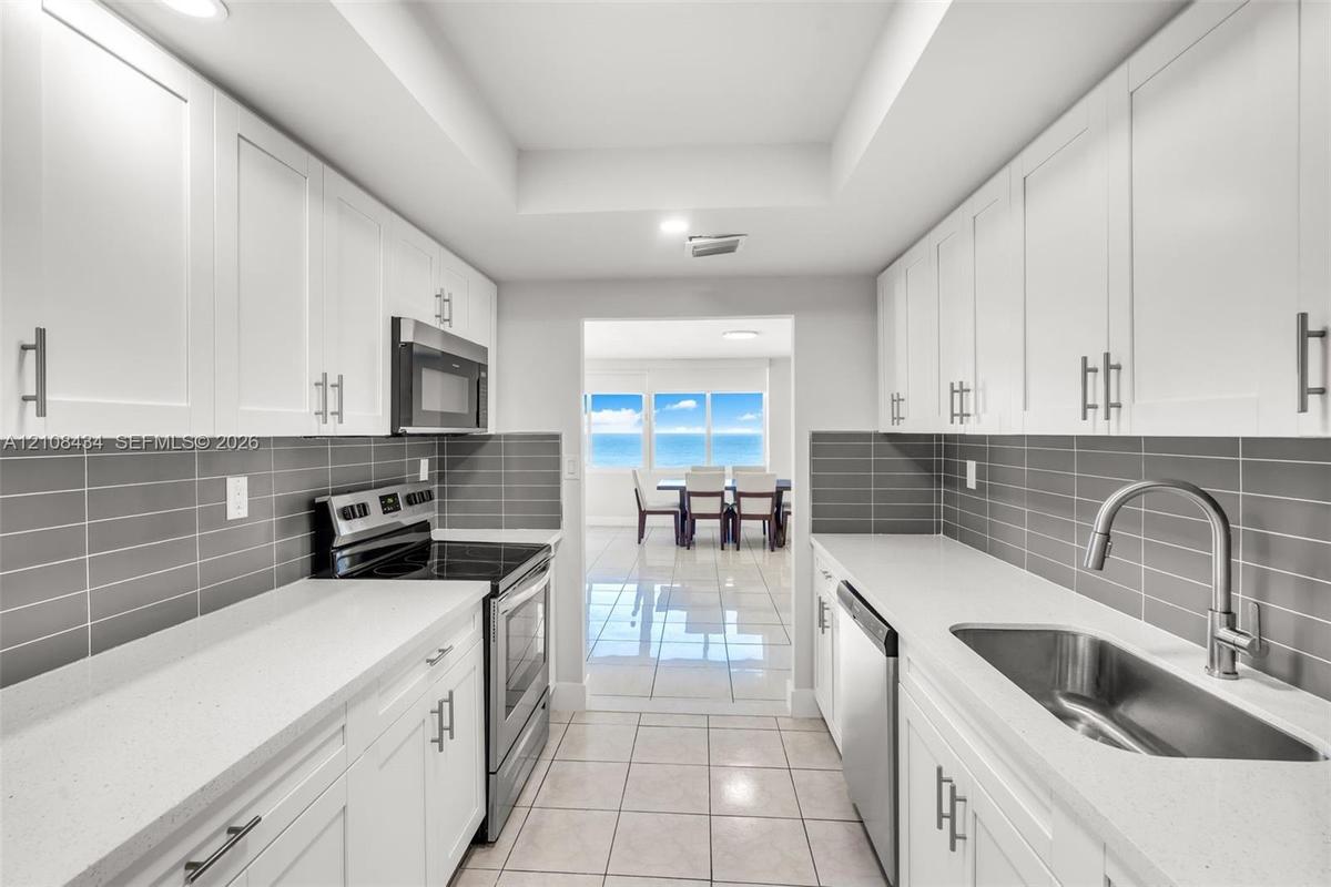 Kitchen featuring white shaker-style cabinetry, solid-surface countertops, horizontal gray tile backsplash, stainless steel appliances, and large-form