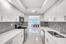 Kitchen featuring white shaker-style cabinetry, solid-surface countertops, horizontal gray tile backsplash, stainless steel appliances, and large-form