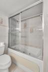 Jetted soaking tub with integrated shower, sliding glass enclosure, and wall-mounted plumbing fixtures surrounded by ceramic tile wall accents