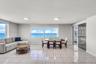 Open-concept room featuring light-toned tile flooring, large multi-pane windows, and a sliding glass door providing access to a balcony with an ocean 